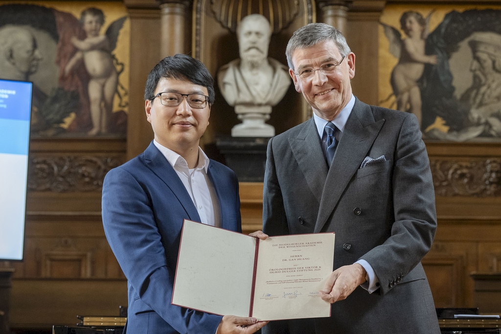Two men holding a certificate in an ornate room with statues and paintings.